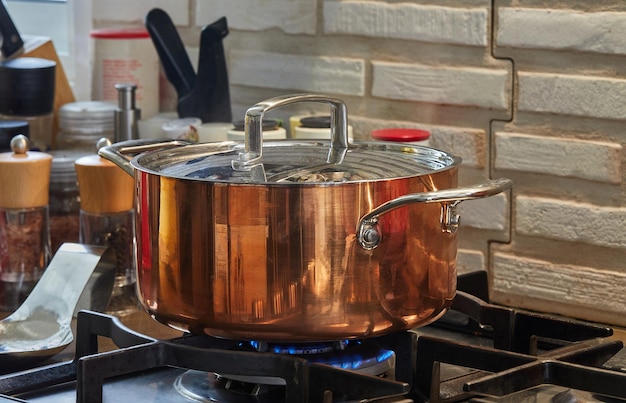 Koperen steelpan met deksel met schotel wordt gekookt boven vuur op gasfornuis Stoom stijgt boven de pot