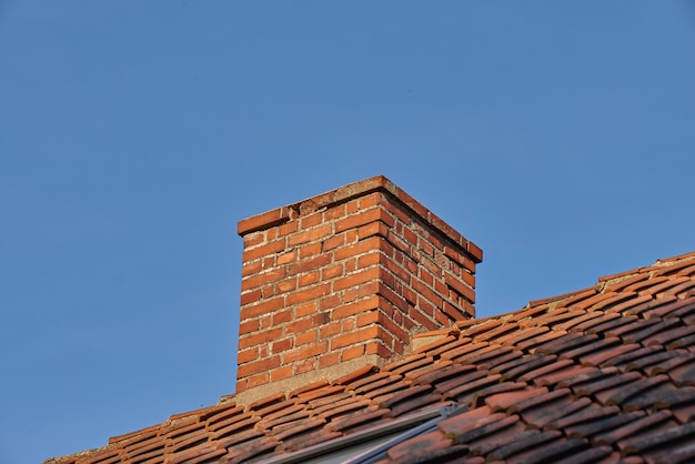 Kopieer de ruimte met een schoorsteen op het dak van een huis of gebouw tegen een blauwe hemelachtergrond Bakstenen constructie van een externe ontsnappingskoker voor ventilatie van lucht en rook van een open haard of oven