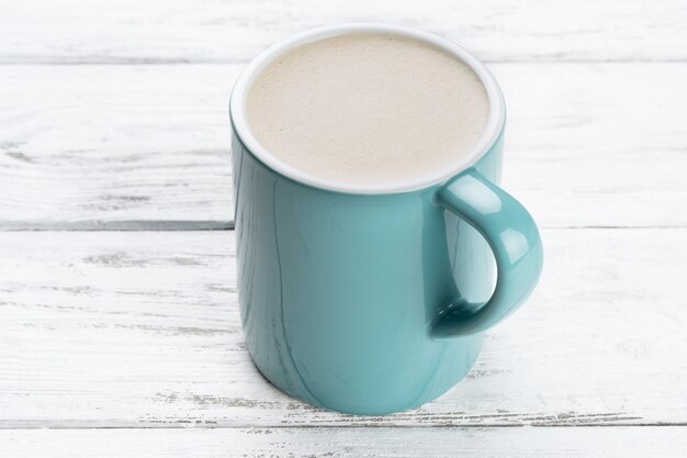 Kopje cappuccino-koffie in een blauwe mok op witte houten achtergrond