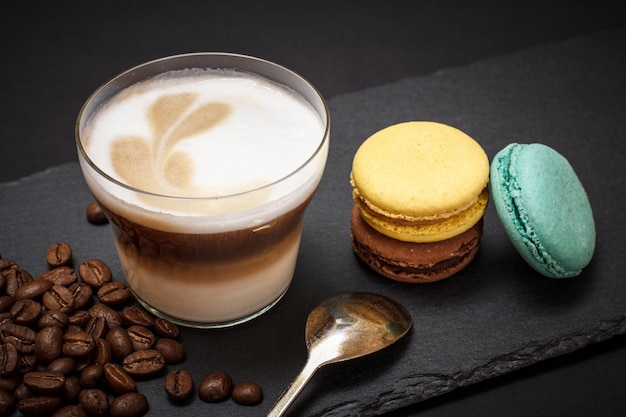 Kopje cappuccino, koffiebonen, lepel en bitterkoekjes op zwarte achtergrond. Bovenaanzicht.