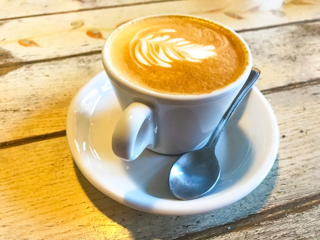 Kopje cappuccino met patroon op oude houten tafel.