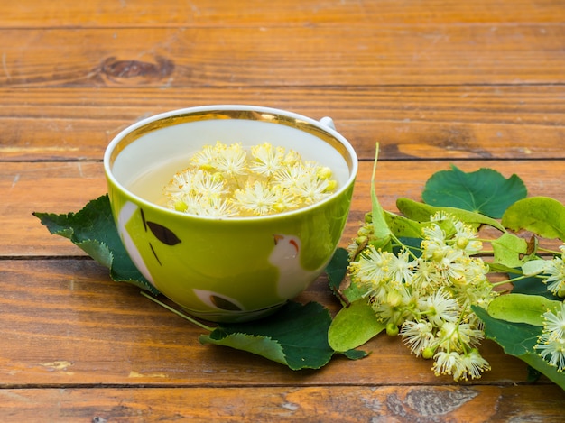 Kopje groene thee en linden op houten achtergrond, nuttige linden bloemen volksgeneeskunde concept