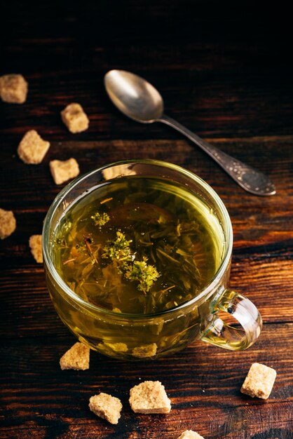 Kopje groene thee met bruine theesuiker op een houten ondergrond