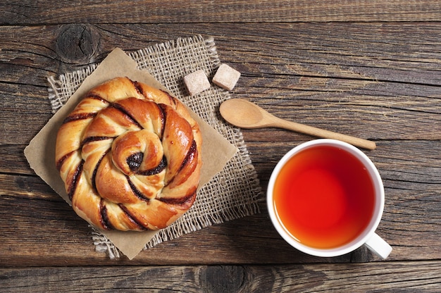 Kopje hete thee en zoet broodje met jam op oude houten tafel, bovenaanzicht