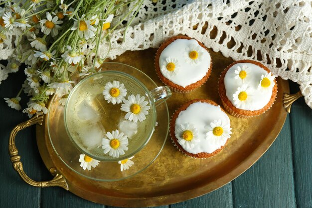 Kopje kamille thee met kamille bloemen en smakelijke muffins op dienblad op een houten achtergrond kleur