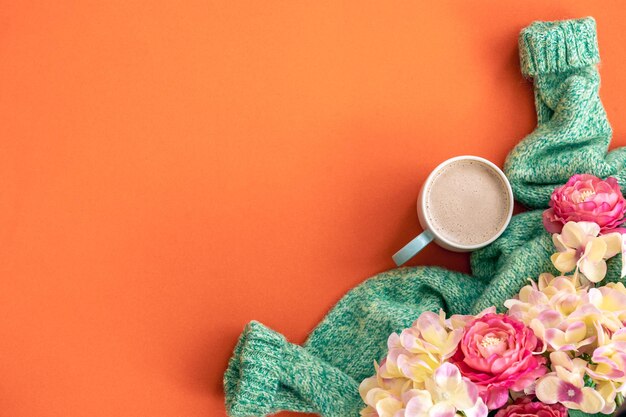 Kopje koffie bloemen en gebreid element op oranje achtergrond plat lag