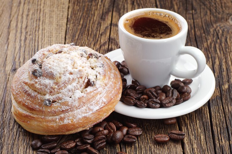 Kopje koffie, broodje en koffiebonen op houten tafel