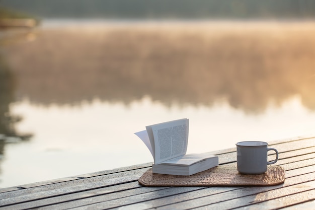 Kopje koffie en boek op houten pier op zomermeer