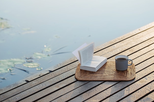 Kopje koffie en boek op houten pier op zomermeer
