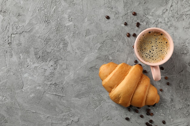 Kopje koffie en croissant op grijze achtergrond, bovenaanzicht