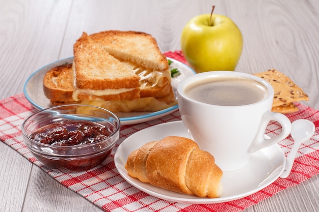 kopje koffie en croissant op schotel glazen kom met aardbeienjam koekjes