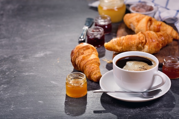 Kopje koffie en croissants met fruitjam op donkere tafel