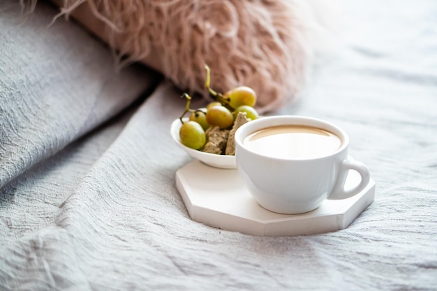Kopje koffie en druiven met gezellig kussen op deken in het interieur van de slaapkamer