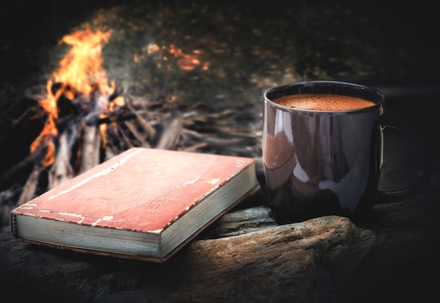 Kopje koffie en een boek met kampvuur nacht achtergrond.