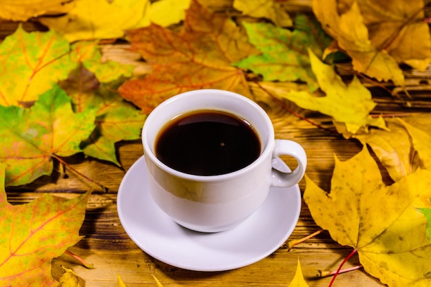 Kopje koffie en een hoop gele esdoornbladeren op een houten tafel