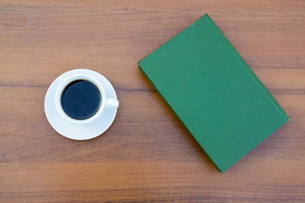 Kopje koffie en gesloten boek op houten tafel. Bovenaanzicht