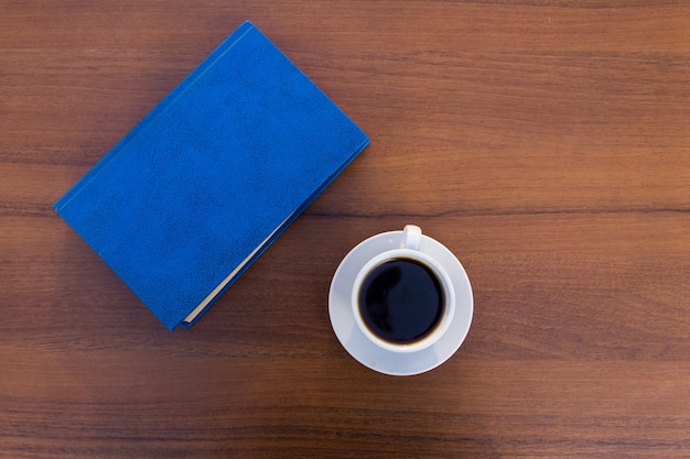 Kopje koffie en gesloten boek op houten tafel. Bovenaanzicht