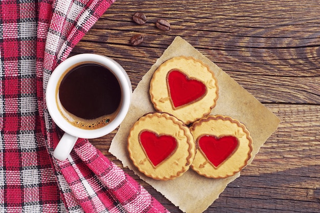 Kopje koffie en koekjes met jam in de vorm van een hart op houten tafel, bovenaanzicht