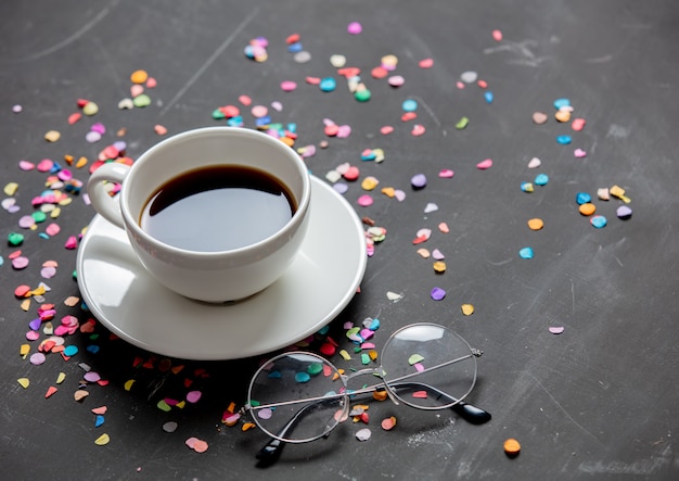 Foto kopje koffie en leesbril met confetti rond op een tafel