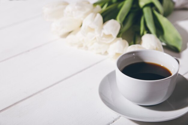 Kopje koffie en witte tulpen op een houten ondergrond