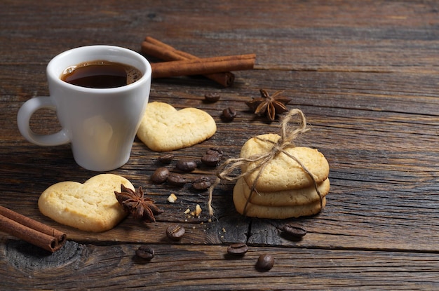 Kopje koffie en zandkoekkoekjes in de vorm van een hart op donkere houten tafel