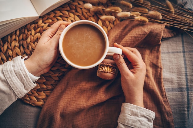 Kopje koffie in handen bovenaanzicht macarons en open boek esthetische foto