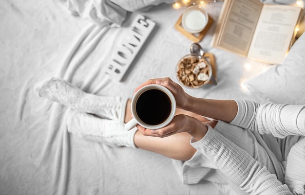 Kopje koffie in vrouwelijke handen in bed bovenaanzicht