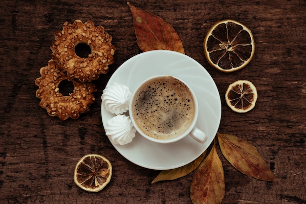 Kopje koffie, koekjes en herfstbladeren op een houten tafel, bovenaanzicht,