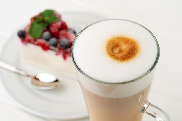 Kopje koffie latte met stuk bessen cheesecake close-up