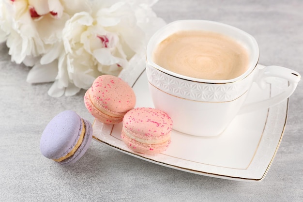 Kopje koffie met bitterkoekjes en pioenrozen op houten tafel