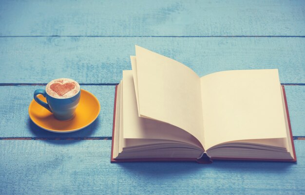 Kopje koffie met boek op blauwe houten tafel.