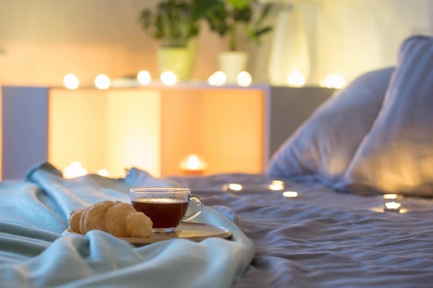 Kopje koffie met croissant op bed in de avond