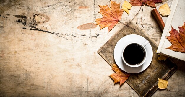 Kopje koffie met een oud boek en esdoornbladeren. Op houten achtergrond.