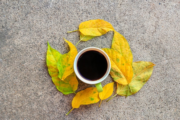 Kopje koffie met herfstbladeren op cementvloer