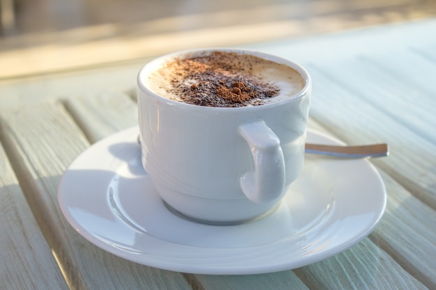 Kopje koffie met latte kunst van cardamon op houten witte tafel.