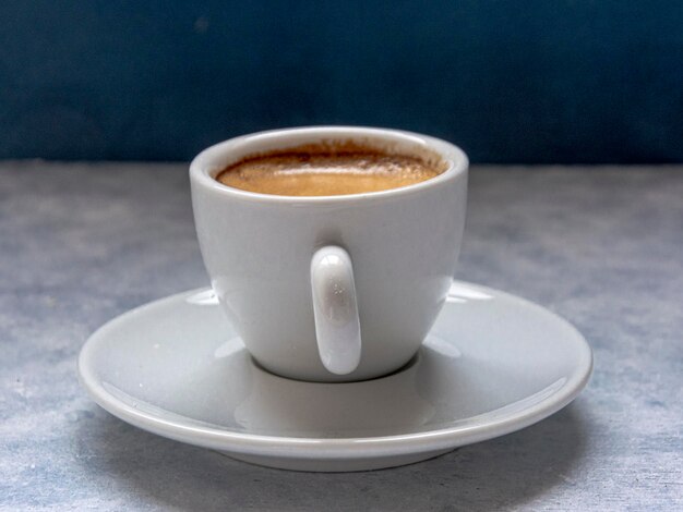 Kopje koffie met lepel op een wit gestructureerd oppervlak voor een blauwe achtergrond. Het heeft een negatieve