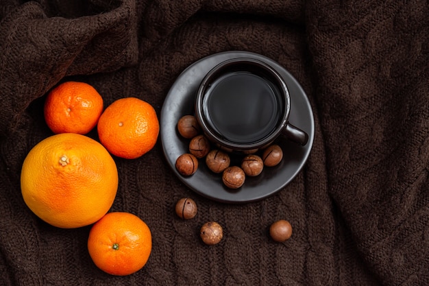 Kopje koffie met mandarijnen en noten op een gebreide bruine dekenachtergrond