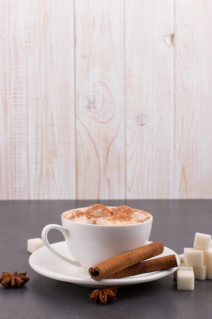 Kopje koffie met marshmallows en cacao, suiker, kaneel en steranijs, op een grijze stenen achtergrond.