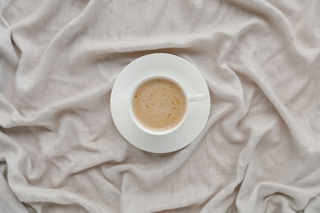 Kopje koffie met melk op het bed met grijs linnen laken ochtendkoffie concept zondag eenzaamheid ontspannen knuffel stemming minimalisme compositie met pastel neutrale kleuren