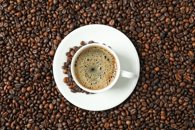 Kopje koffie met schuimige schuim op bonen achtergrond