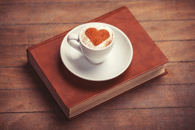 Kopje koffie met vormhart en boek op een houten tafel