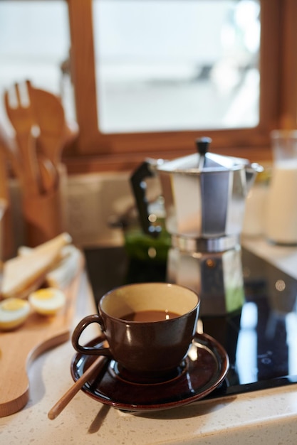 Kopje koffie op aanrecht naast fornuis met mokkapot erop