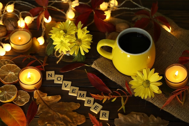 Kopje koffie op de herfstachtergrond met bladeren en bloemen. tekst november