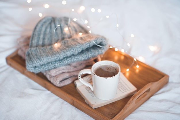 Kopje koffie op open boek dat op een houten dienblad blijft met gebreide kleding van dichtbij boven kerstverlichting goedemorgen winterseizoen