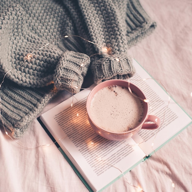 Kopje koffie op open boek met gebreide textiel in bed close-up. Winter vakantie seizoen. Ontbijt.