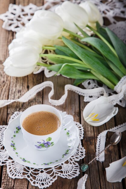 Kopje koffie op oude houten achtergrond en een boeket van witte tulpen.