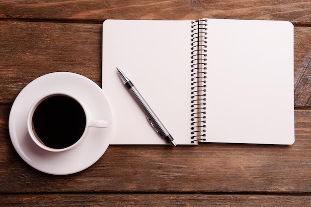 Kopje koffie op schotel met notitieboekje en pen op houten tafel achtergrond