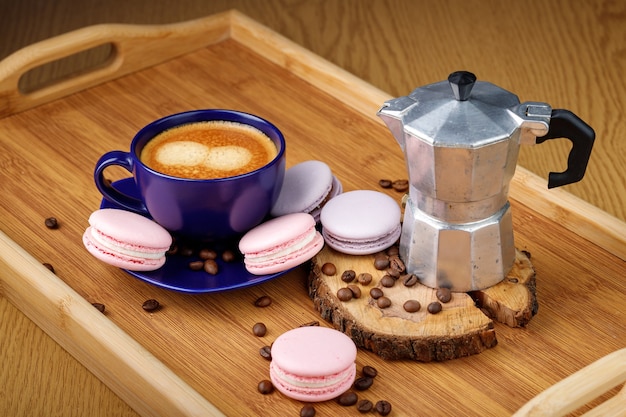 Kopje koffie, roze bitterkoekjes en koffiebonen op een schotel op een houten dienblad