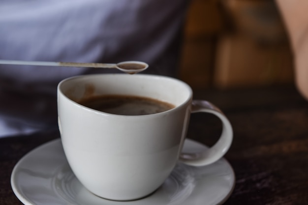 Kopje koffie vastgehouden door een mannenhand, terwijl op houten tafelblad.