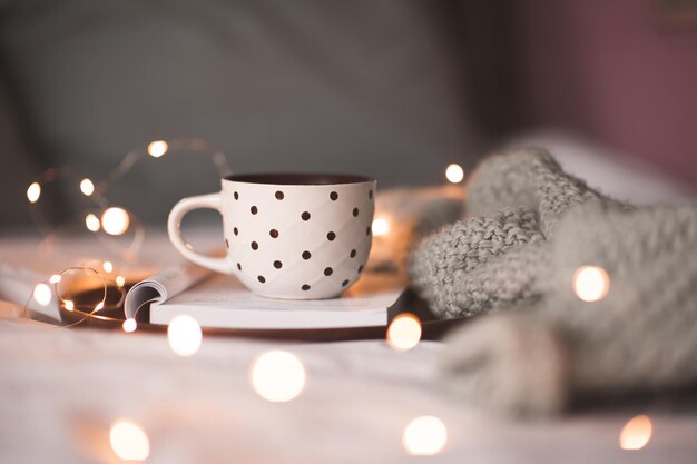 Kopje koffie verblijf op open boek met aangekleed textiel in bed close-up. Goedemorgen. Winter vakantie seizoen.